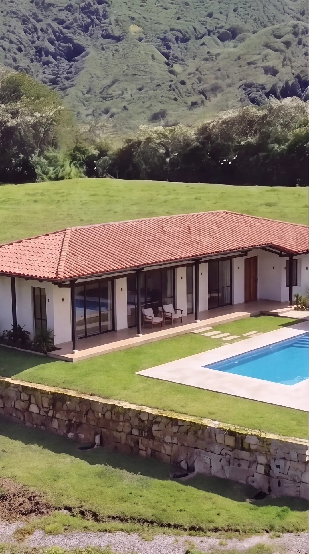 Fachada de la casa campestre de teja, con corredor y una piscina pequeña al lado, sobre un lote del proyecto, de día.